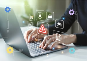 Hands typing on a laptop with icons of gears, file folders, and a warning.