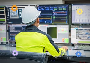 A person wearing a hard hat looking at multiple computer monitors.
