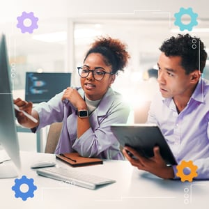 Two people looking at a computer monitor while one holds a tablet.